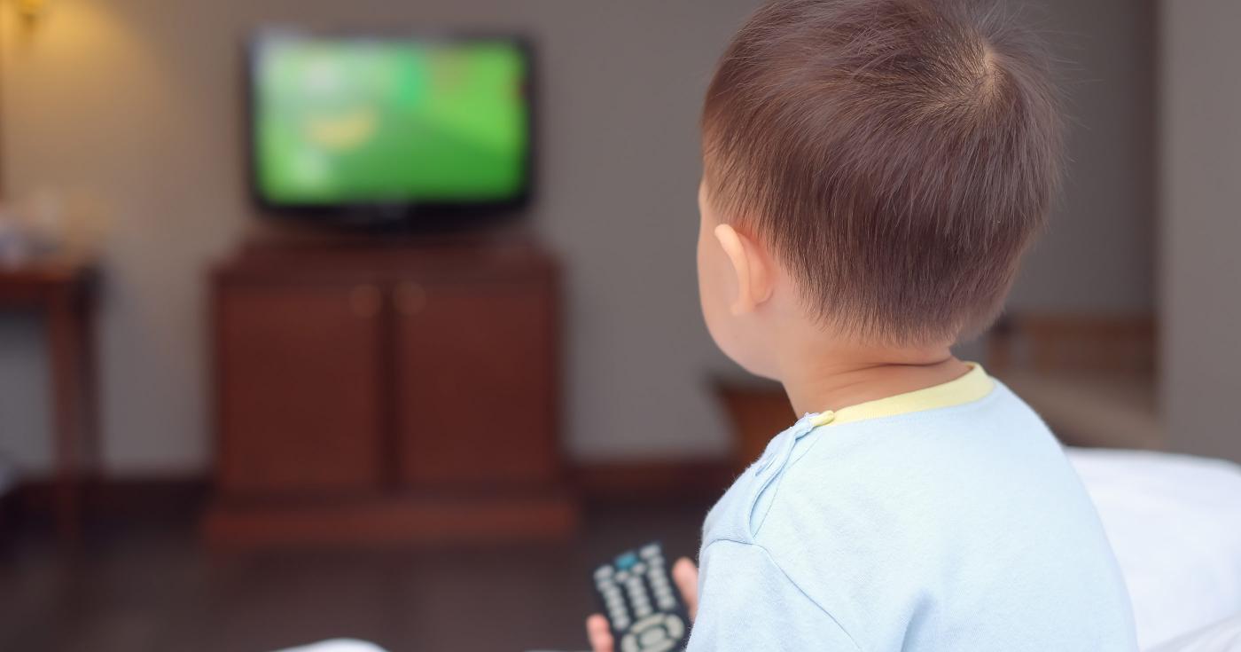 Moins d’écrans ? Un jeu d’enfant ! Bébé devant la télévision avec une télécommande dans la main